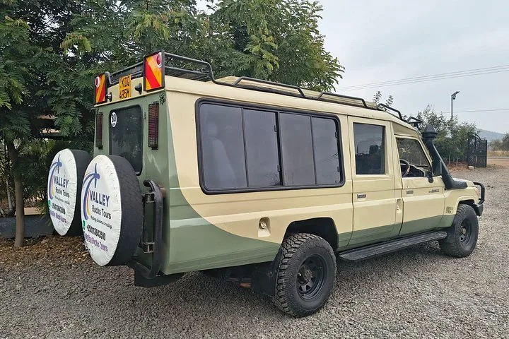 Ein geparktes beiges und grünes Safari-Fahrzeug mit Ersatzreifen hinten.
